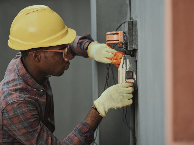 A technician in a yellow hard hat and gloves working on equipment.